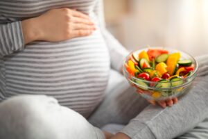 A pregnant woman holding a bowl of healthy vegetables and fruits