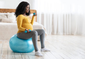 A pregnant woman exercises with light weights and an exercise ball to stay active